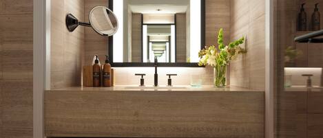 A modern bathroom with a large mirror, a sink with two faucets, and a vase with flowers.