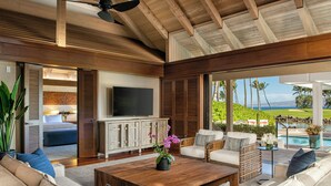 A spacious living area with a large wooden coffee table, comfortable seating, a flat-screen TV, and a view of the ocean. - Mauna Lani, Auberge Collection (Kamuela)