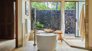 A bathroom with a large bathtub, a stone wall, and a view of greenery.