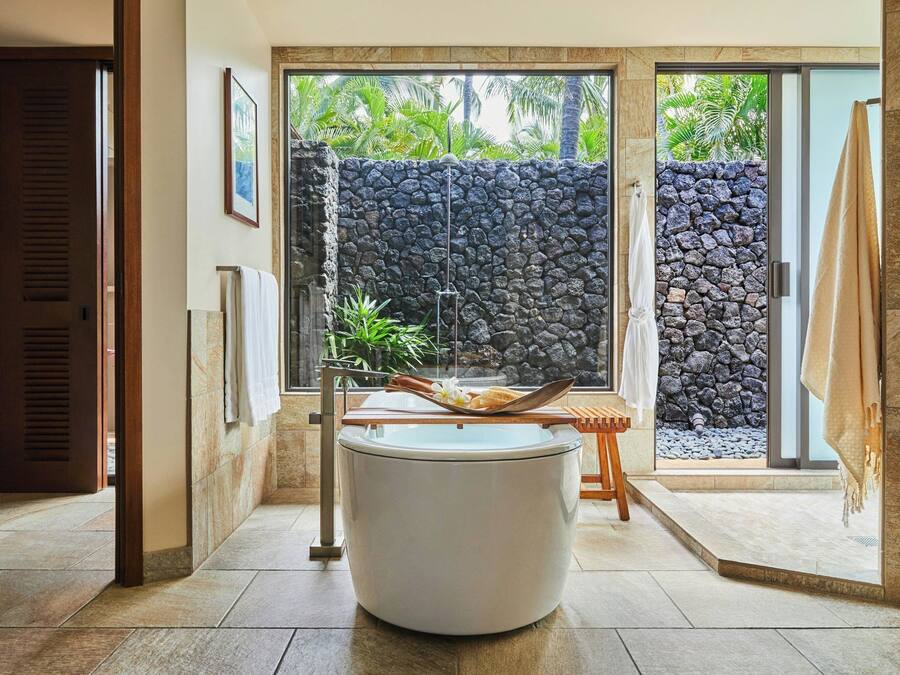 A bathroom with a large bathtub, a stone wall, and a view of greenery.