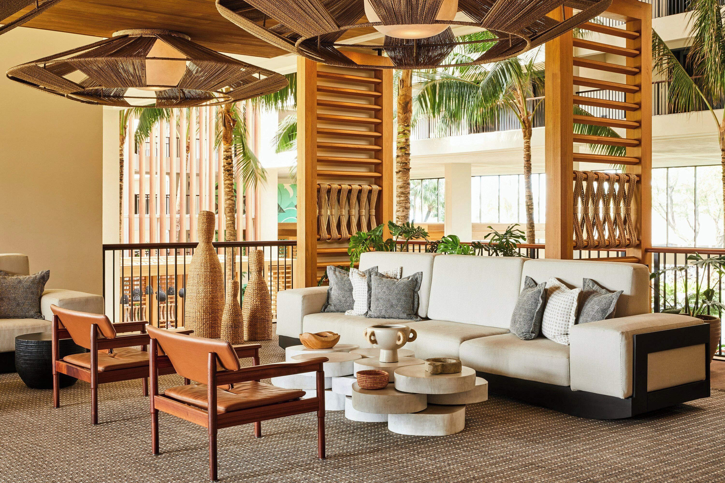 A modern lounge area with a sofa, chairs, and a coffee table, featuring natural light and indoor plants.