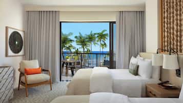 A hotel room with a balcony, a bed, a chair, a table, and a view of palm trees and the ocean.