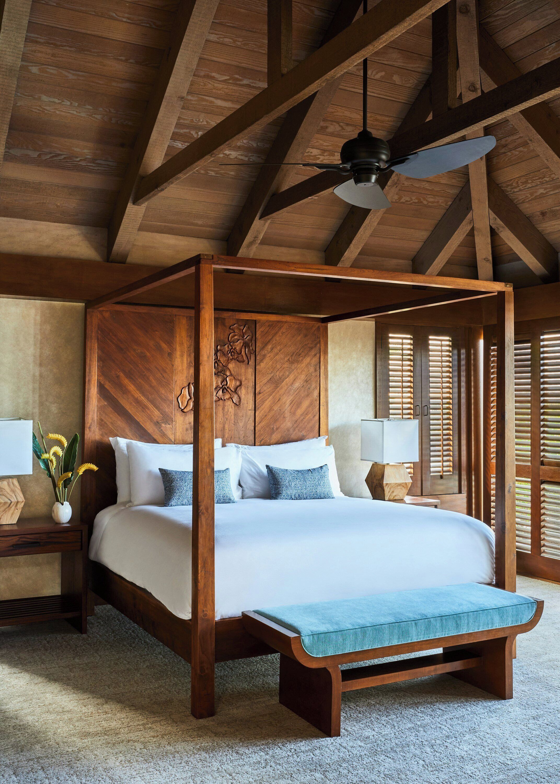 Una cama con dosel con cabecera de madera, una mesita de noche con lámpara y un banco al pie de la cama.