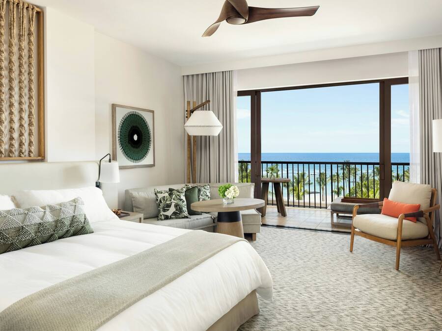 Een hotelkamer met een bed, een bank, een stoel, een tafel en een balkon met uitzicht.