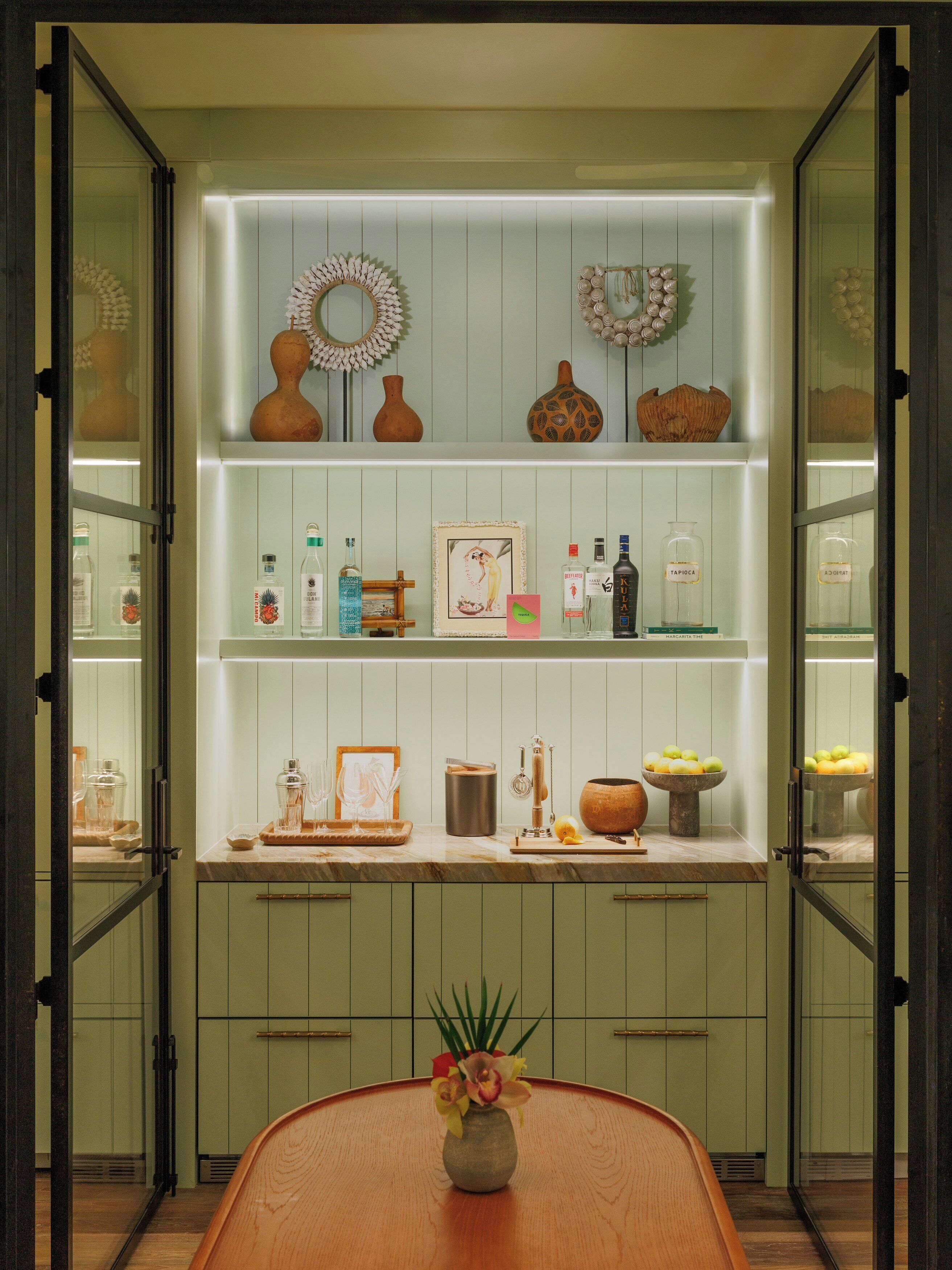 A kitchen with open cabinets displaying various items, a central island with a vase, and a wall-mounted shelf with decorative items.