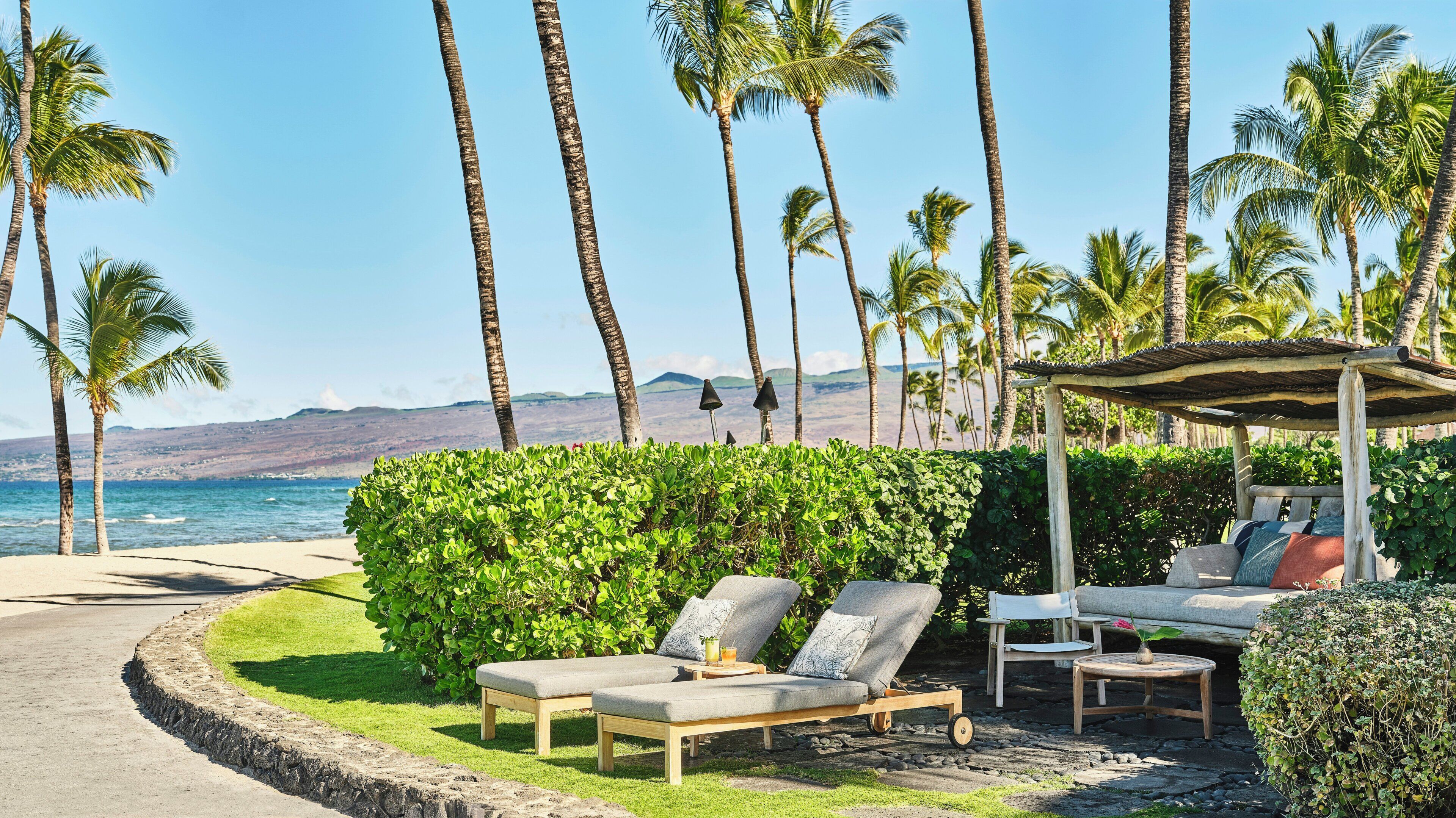 Eine Strandlounge mit Liegestühlen, einem kleinen Tisch mit einem Getränk und einer Pergola.