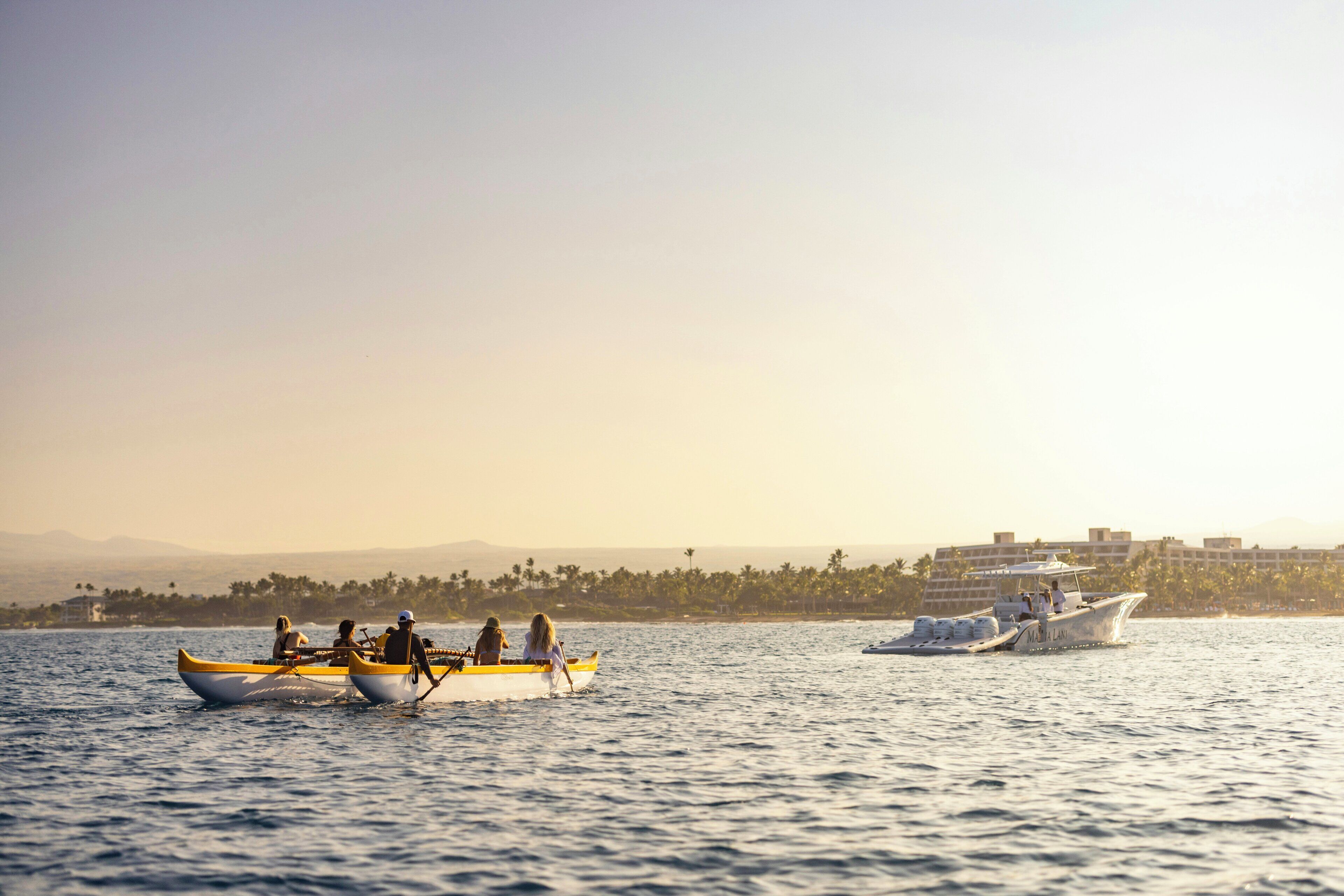 A calm body of water with boats, a distant shoreline with buildings, and a clear sky.