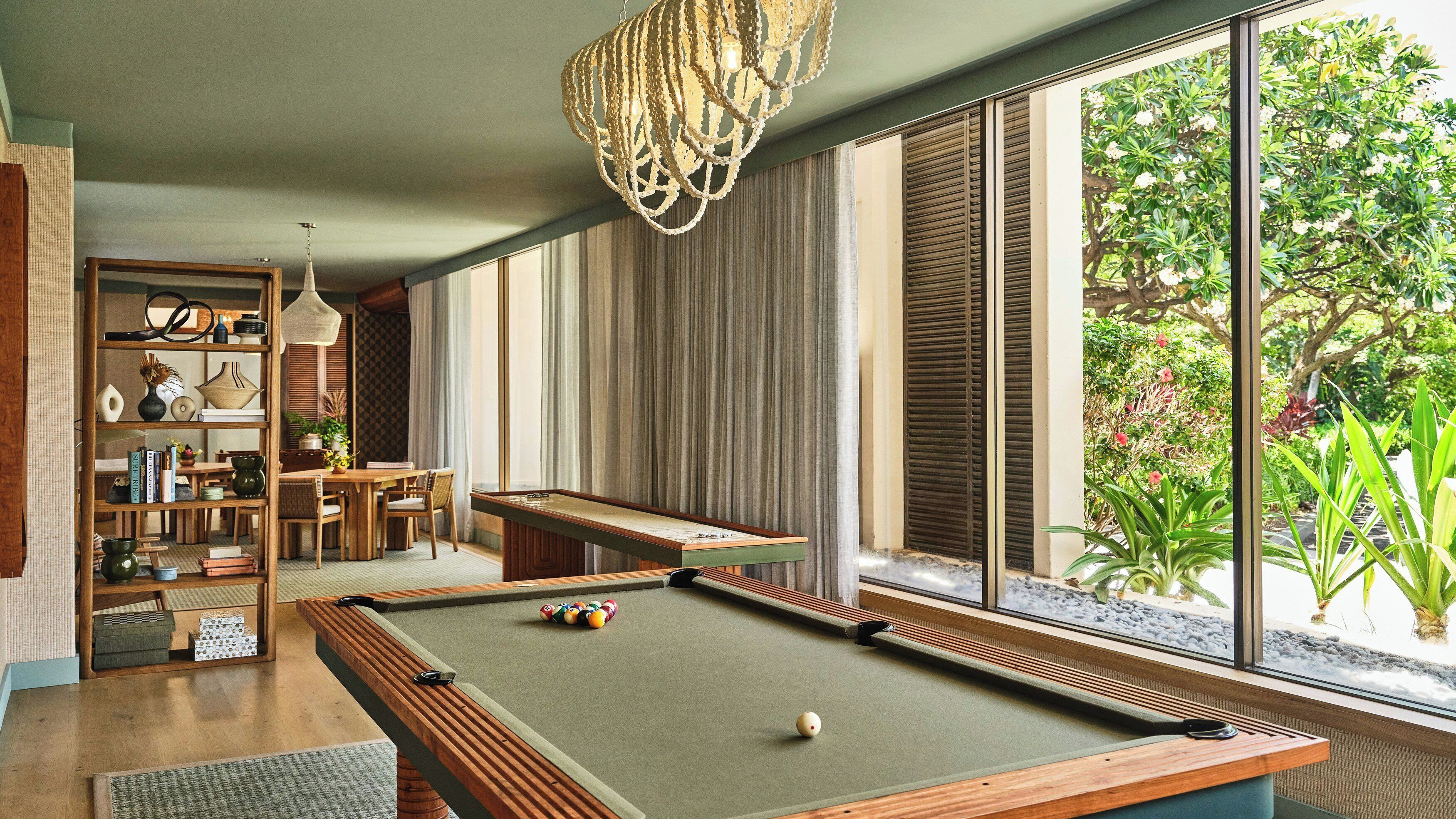 Una mesa de billar con superficie de fieltro verde, rodeada de muebles de madera y una estantería.