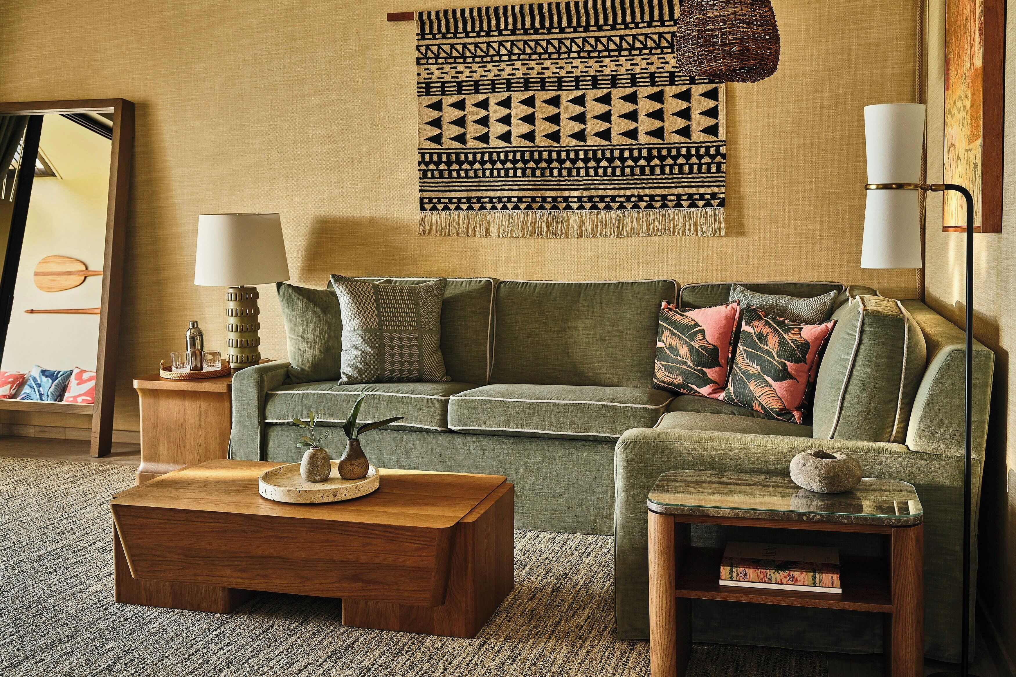 A living room with a green sofa, a wooden coffee table, a small side table, a wall hanging, and a lamp.