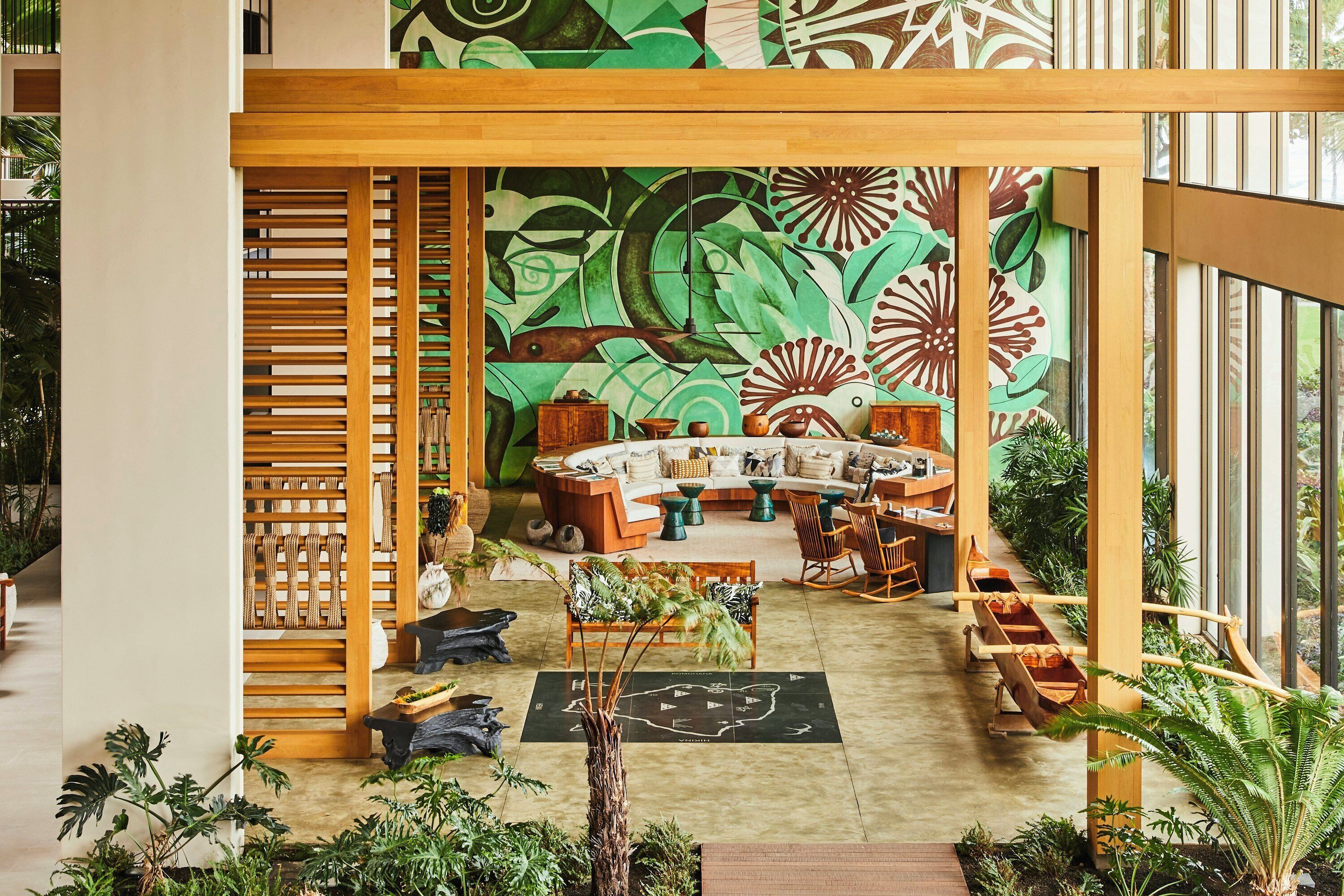 A spacious lobby with a central seating area, a large mural, and a variety of plants.
