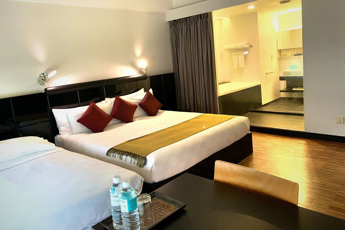 A hotel room with two beds, a bedside table with water bottles, a mirror, and a view of the bathroom.