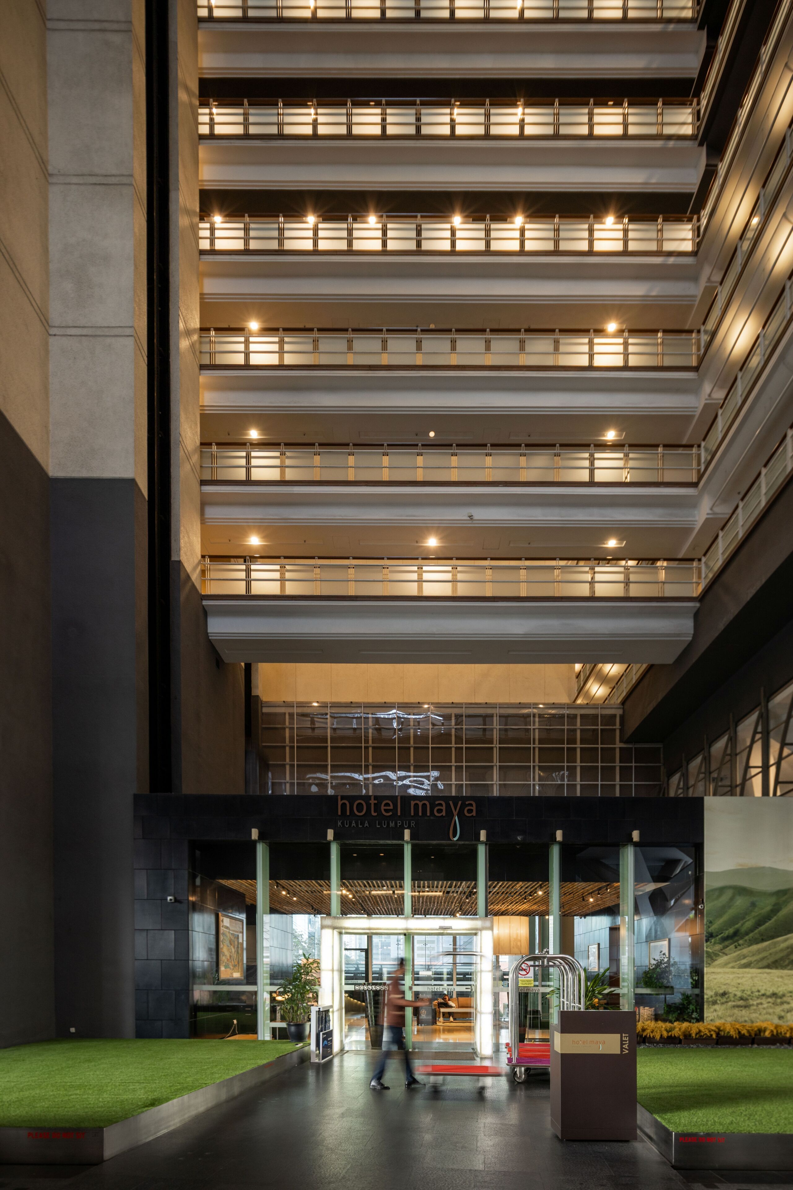 L’entrée d’un hôtel au design moderne, avec une façade en verre et une enseigne indiquant « hôtel Maya ».