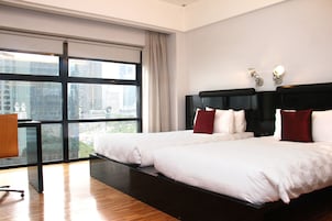 A modern hotel room with two beds, a desk, and a large window offering a city view.