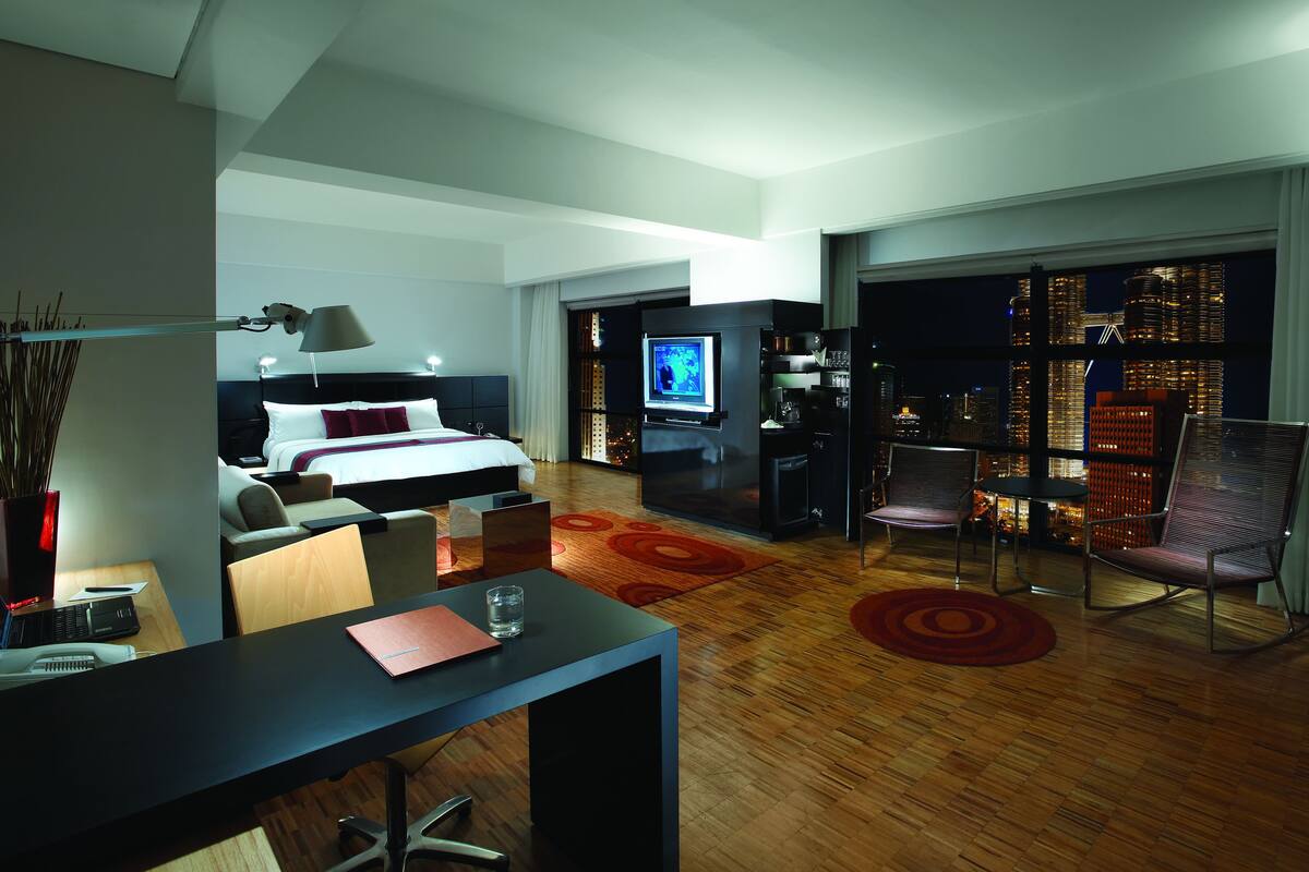 A modern hotel room with a bed, desk, chair, TV, and a city view through the window.