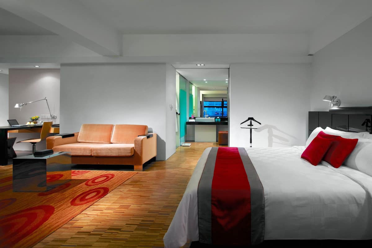 A modern hotel room with a bed, a sofa, a desk with a laptop, and a view of the city through the window.