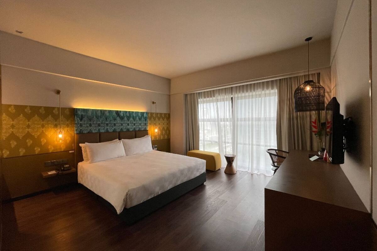 A modern hotel room with a large bed, a desk, and a window with curtains.