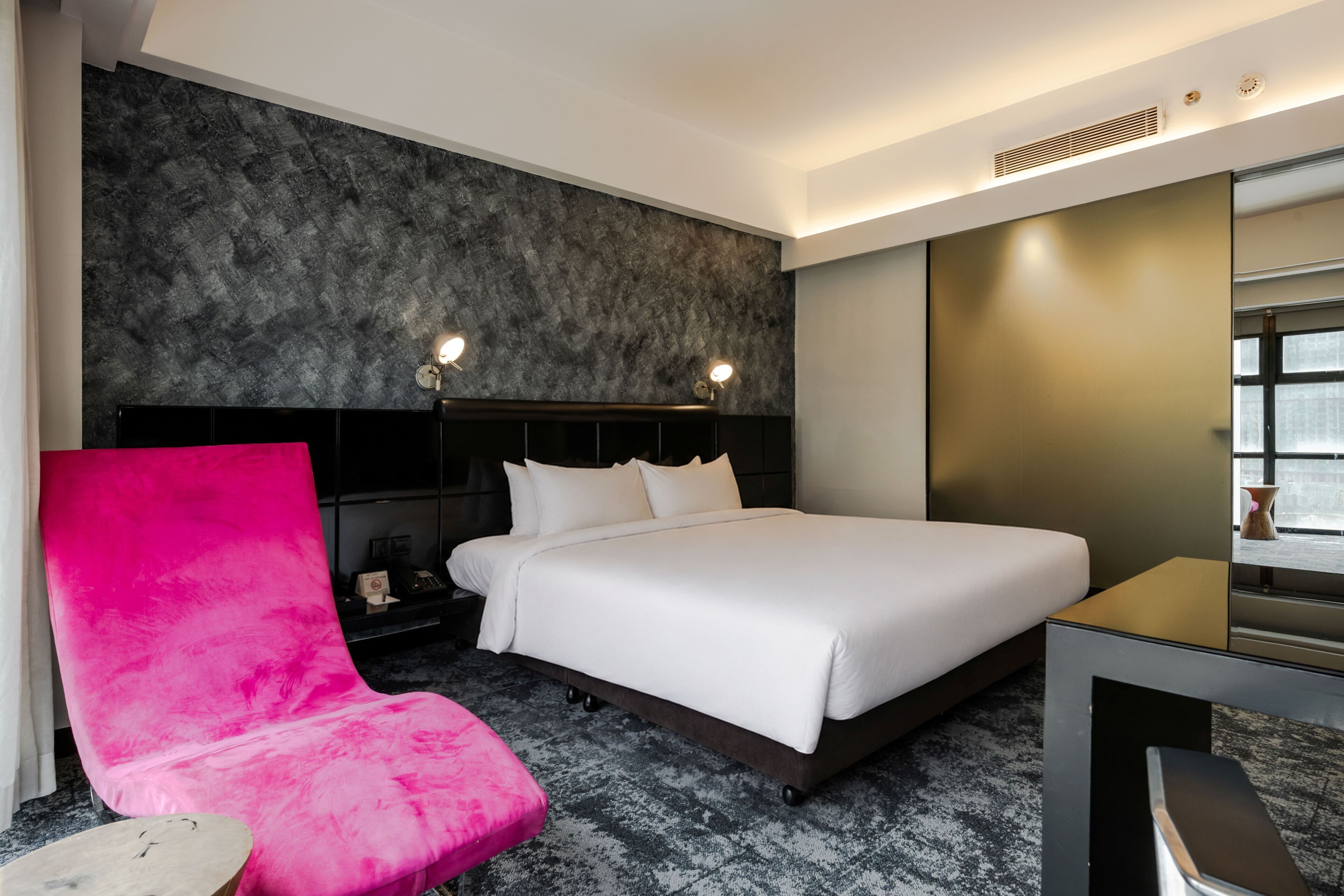 Una habitación de hotel con cama, mesita de noche, silla, escritorio y un espejo grande.