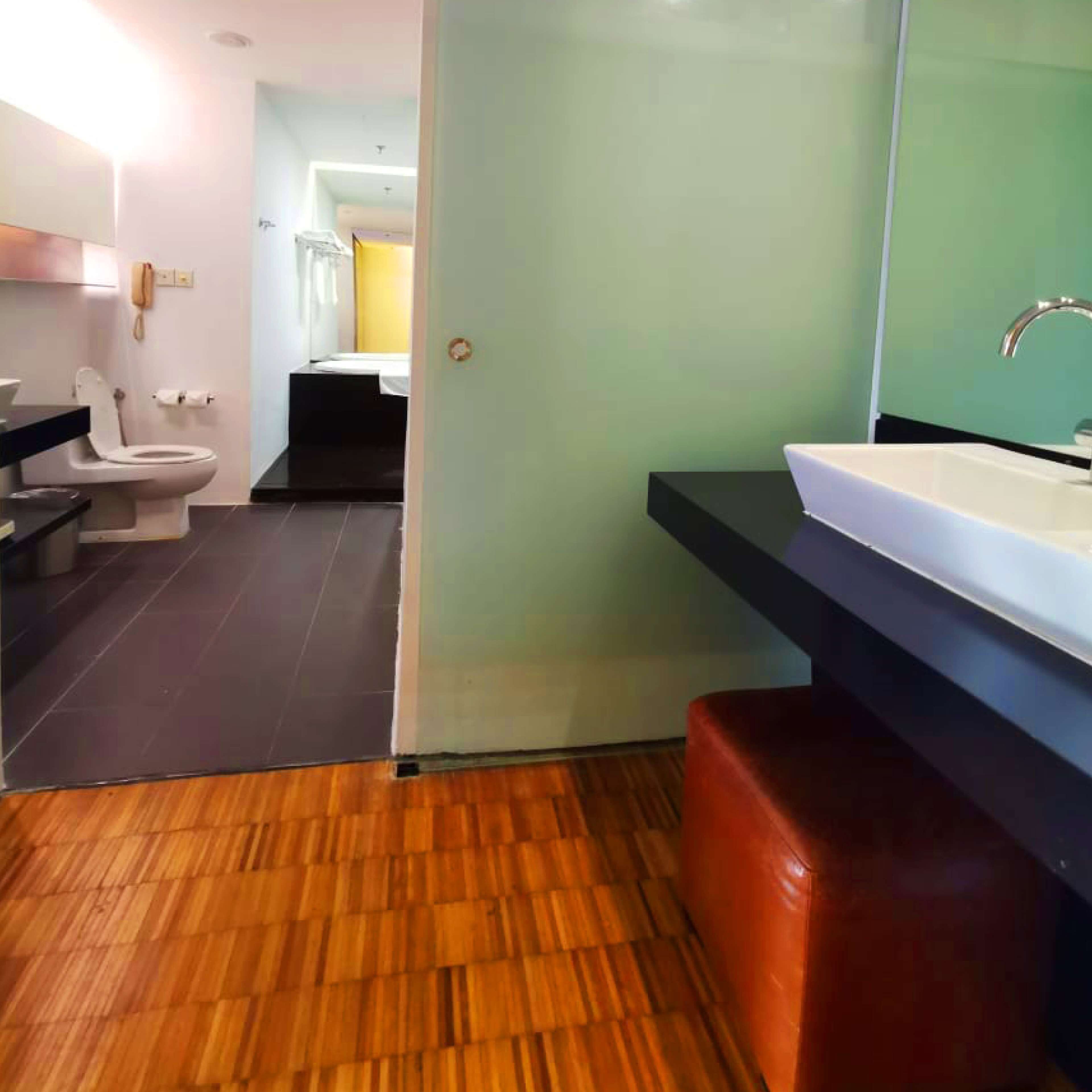 A modern bathroom with a wooden floor, a white toilet, a black sink, and a mirror.
