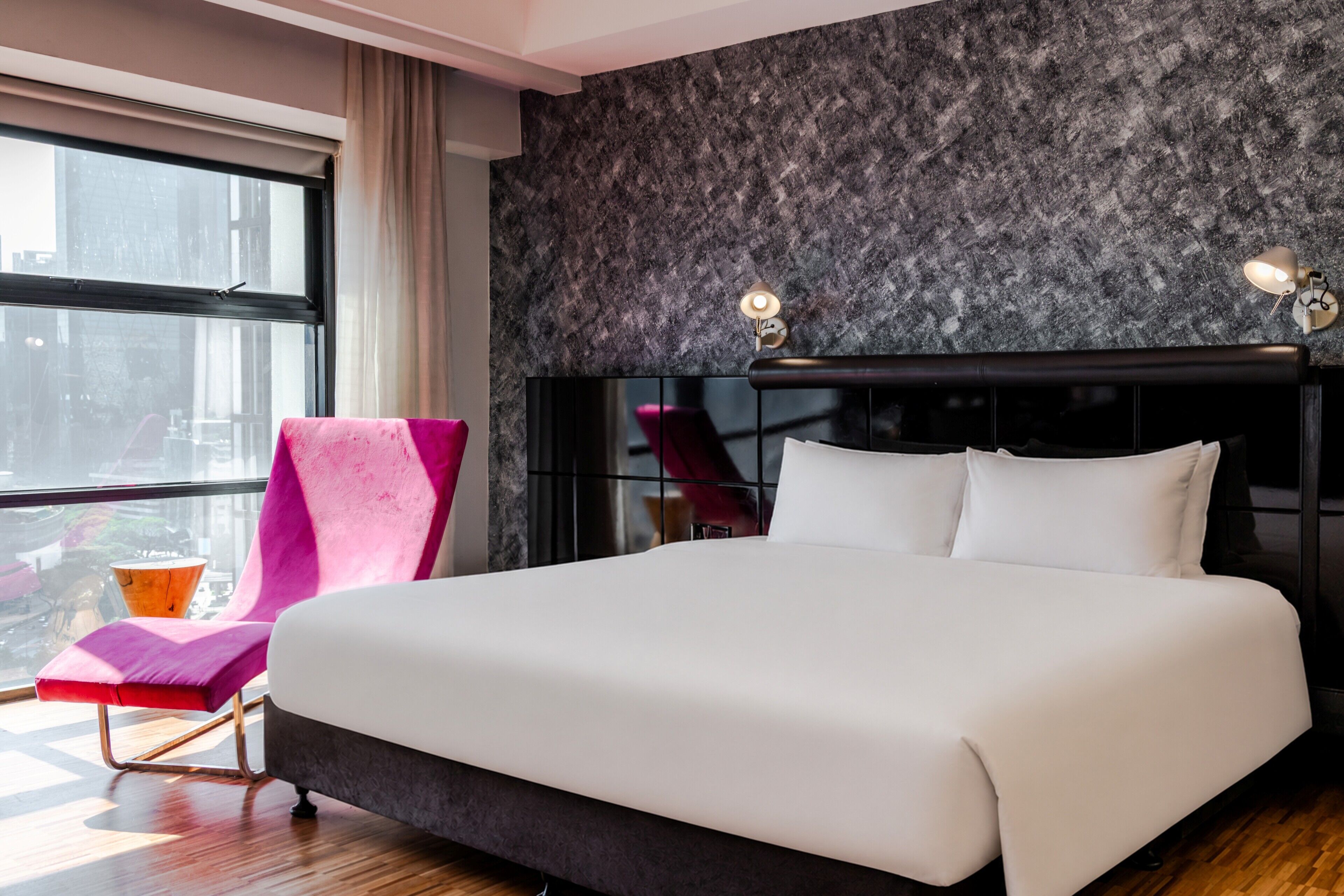 A modern hotel room with a large bed, a chair, and a view of the city.