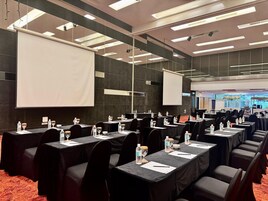 A conference room with rows of tables, chairs, and a large screen.