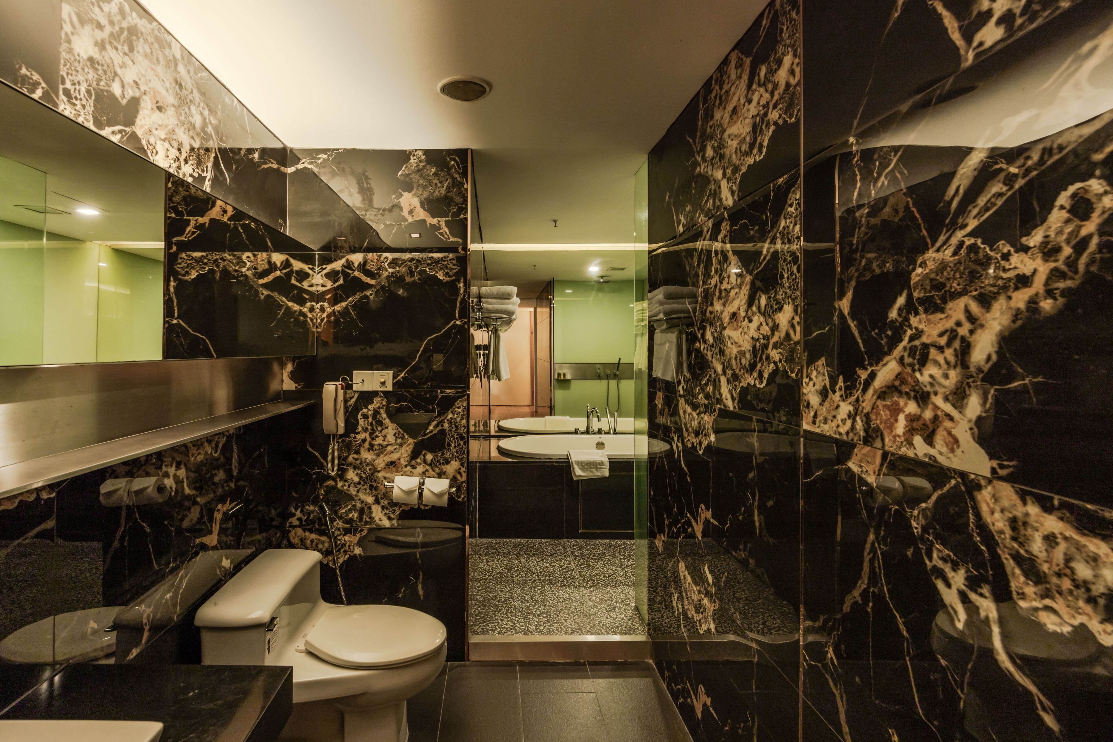 Un baño moderno con inodoro, lavamanos y zona de ducha, con paredes de mármol y mampara de vidrio.