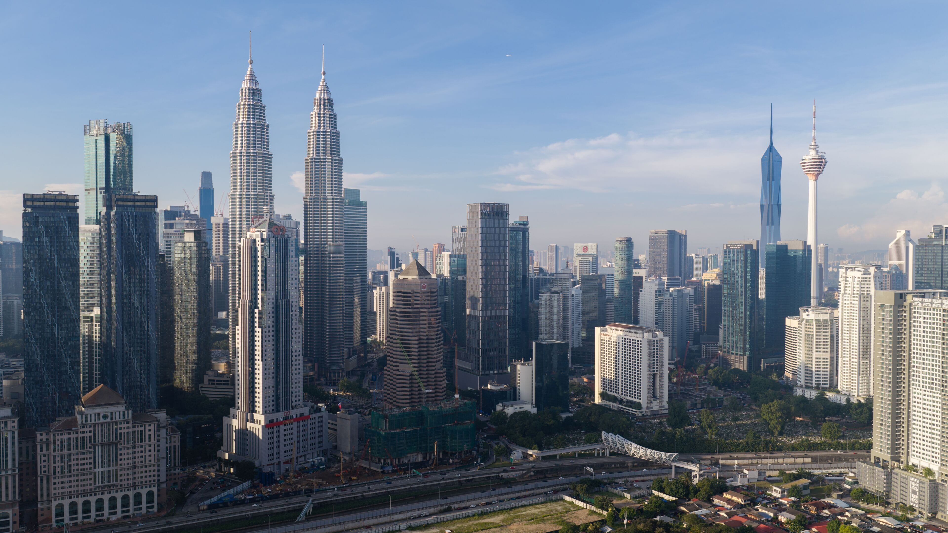 A cityscape with multiple high-rise buildings, including the Petronas Towers and a distinctive tower with a spire.