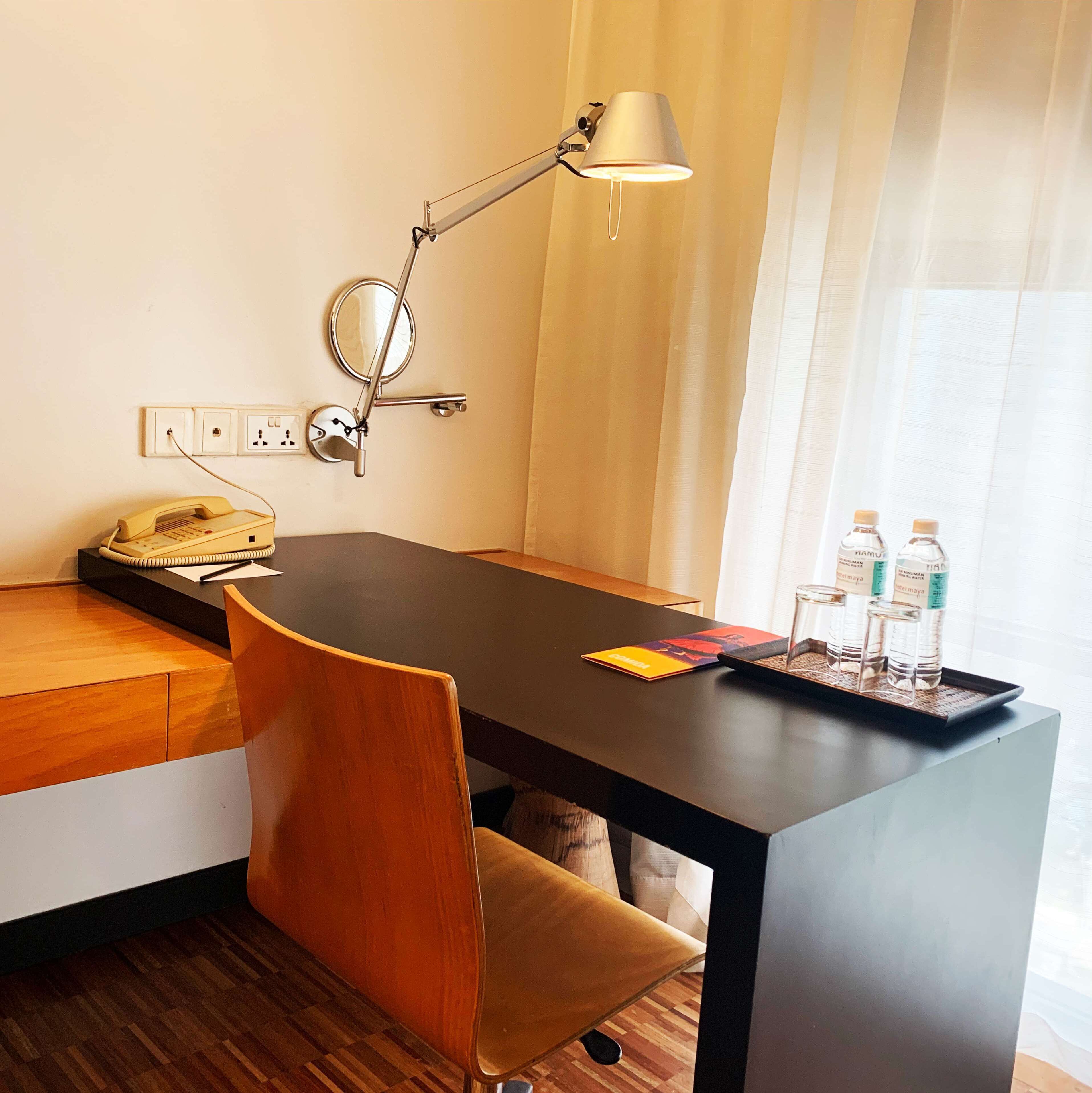 A hotel room with a desk, a telephone, a lamp, and a tray with bottles and glasses.