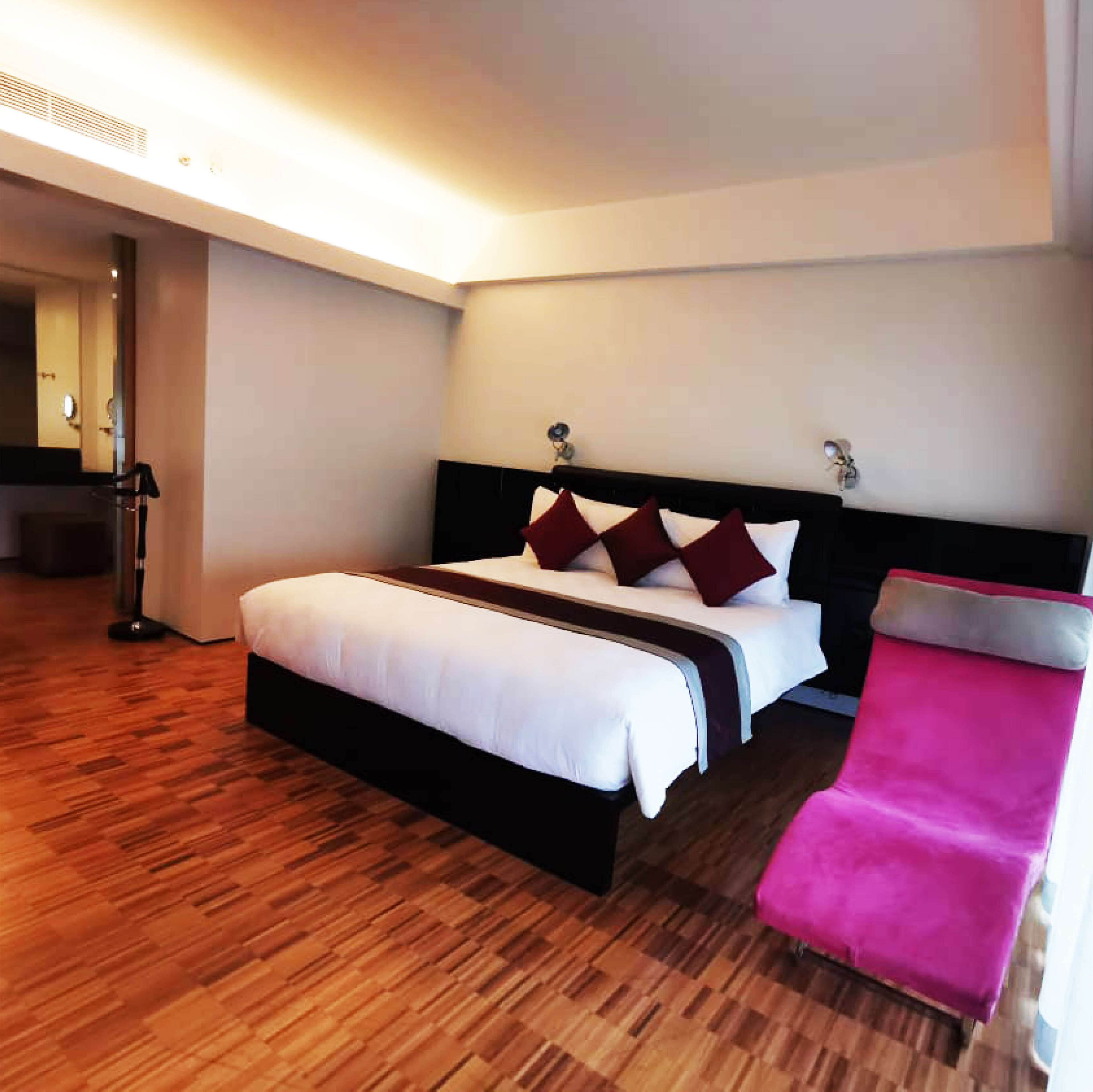 A hotel room with a large bed, a bedside table, a chair, and a mirror.