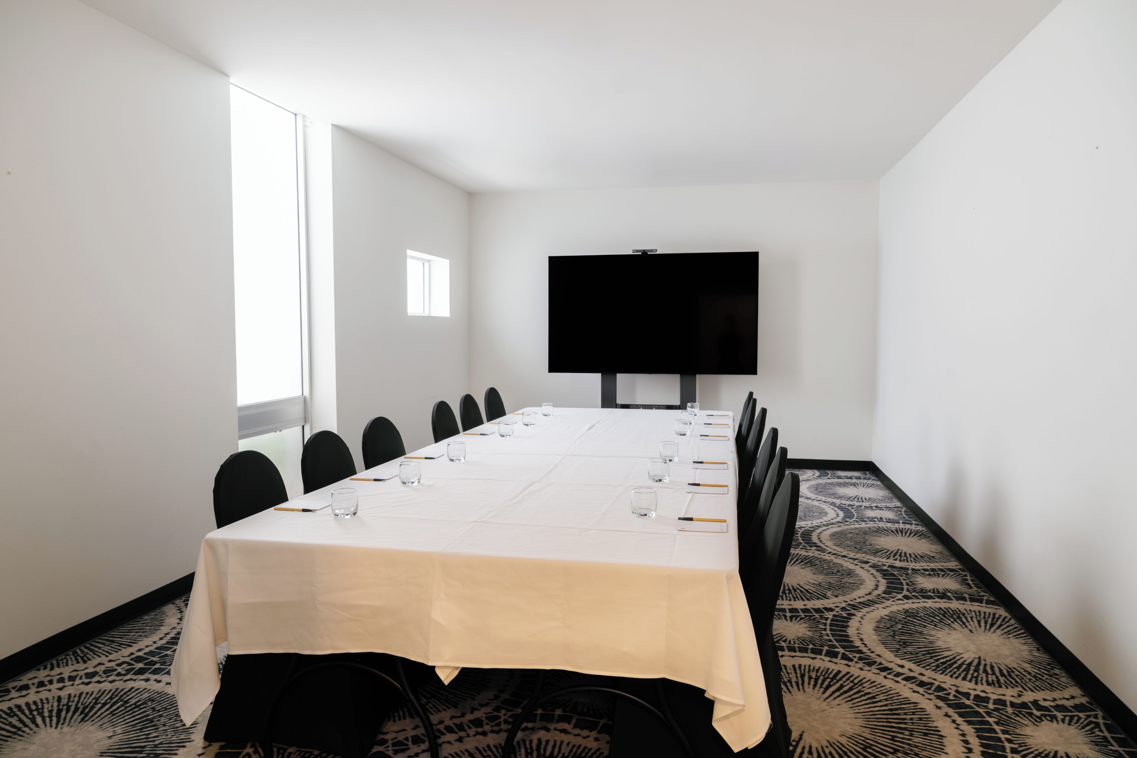 A conference room with a long table, chairs, a TV screen, and patterned carpet.
