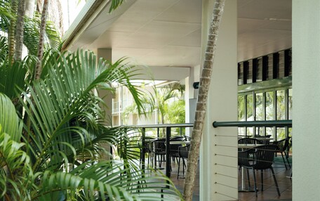 An indoor patio area with tables and chairs, surrounded by palm trees and a view of the outside.