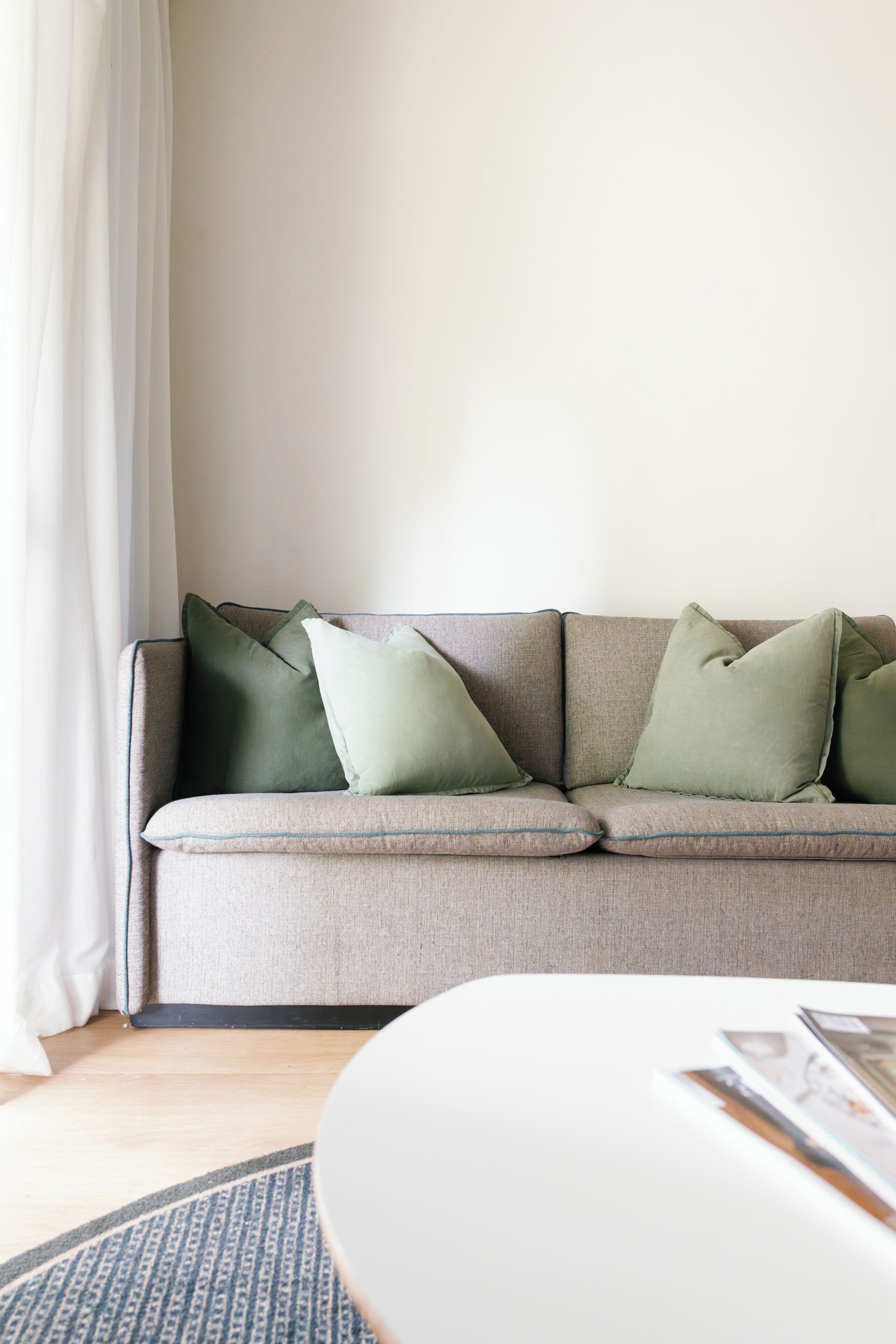 A neutral-toned sofa with green cushions, a white side table, and a patterned rug.