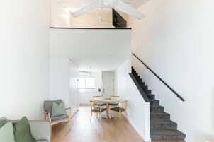 Un interior moderno con zona de comedor, escalera y cocina al fondo.