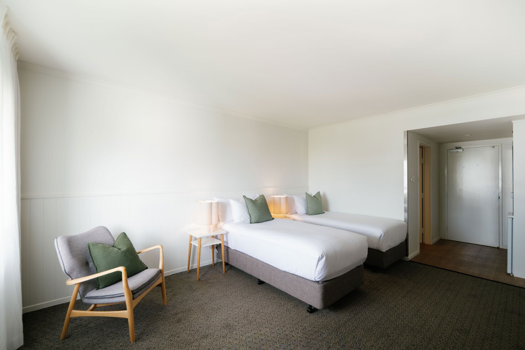 A hotel room with a bed, two bedside tables, a chair, and a door.