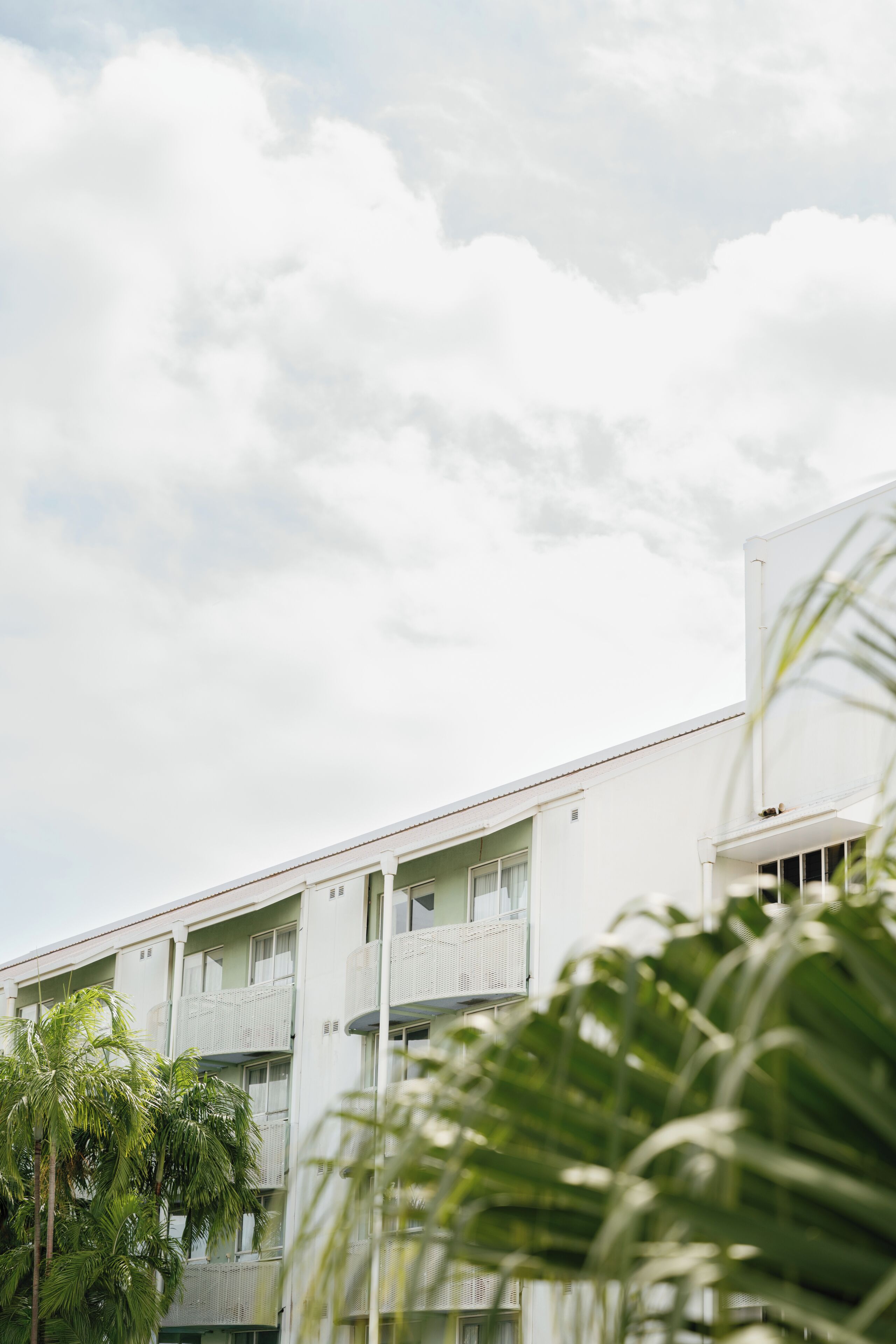 A multi-story building with balconies, surrounded by palm trees.