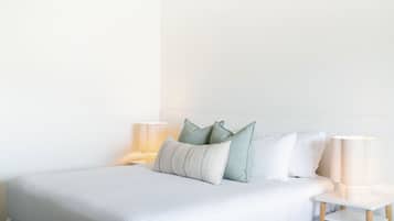 A neatly made bed with pillows and a bedside lamp, a white headboard, and a white nightstand with a lamp.