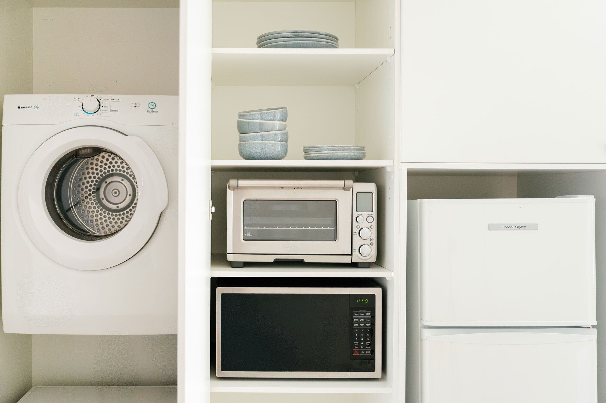 A compact kitchen with a washing machine, a microwave, a toaster oven, and a refrigerator.