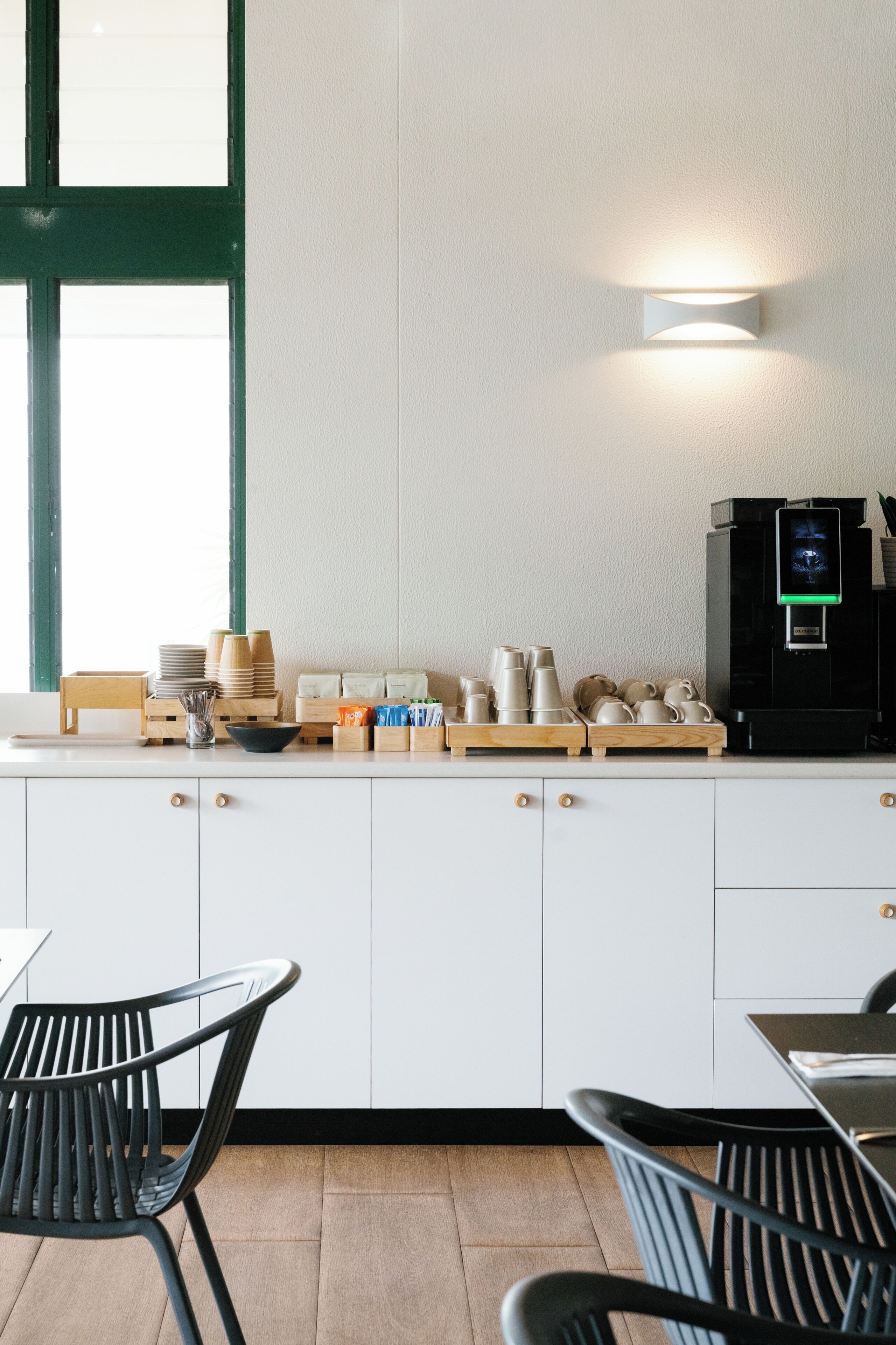 Una cucina moderna con mobili bianchi, una macchina da caffè e una finestra con stipiti verdi.