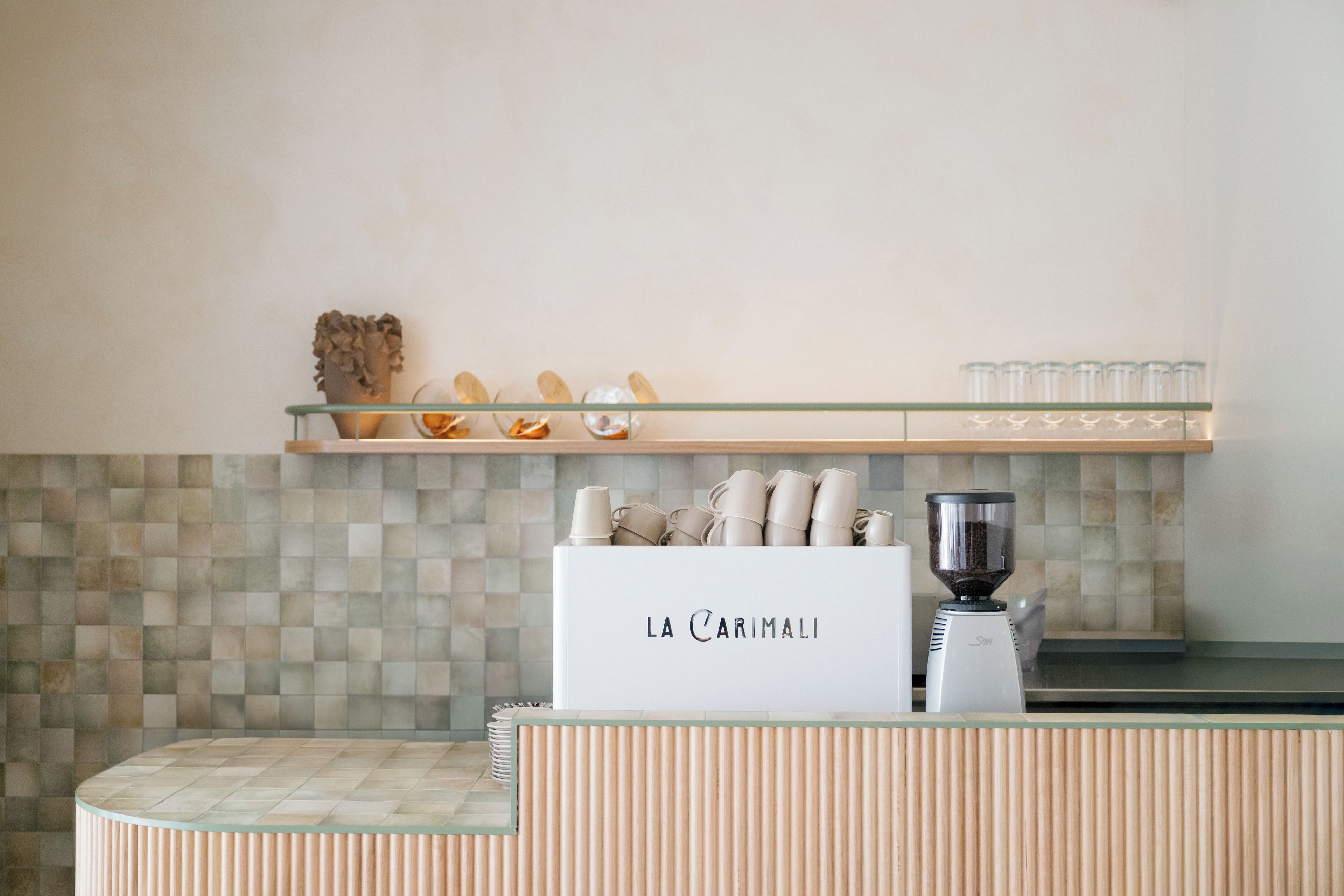 Una encimera de cocina con una cafetera, una vitrina con tazas de café, y un letrero que dice 'LA CARIMALI'.