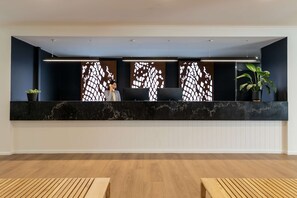 Una zona de recepción con mostrador de mármol, dos plantas en macetas y un muro con diseño.