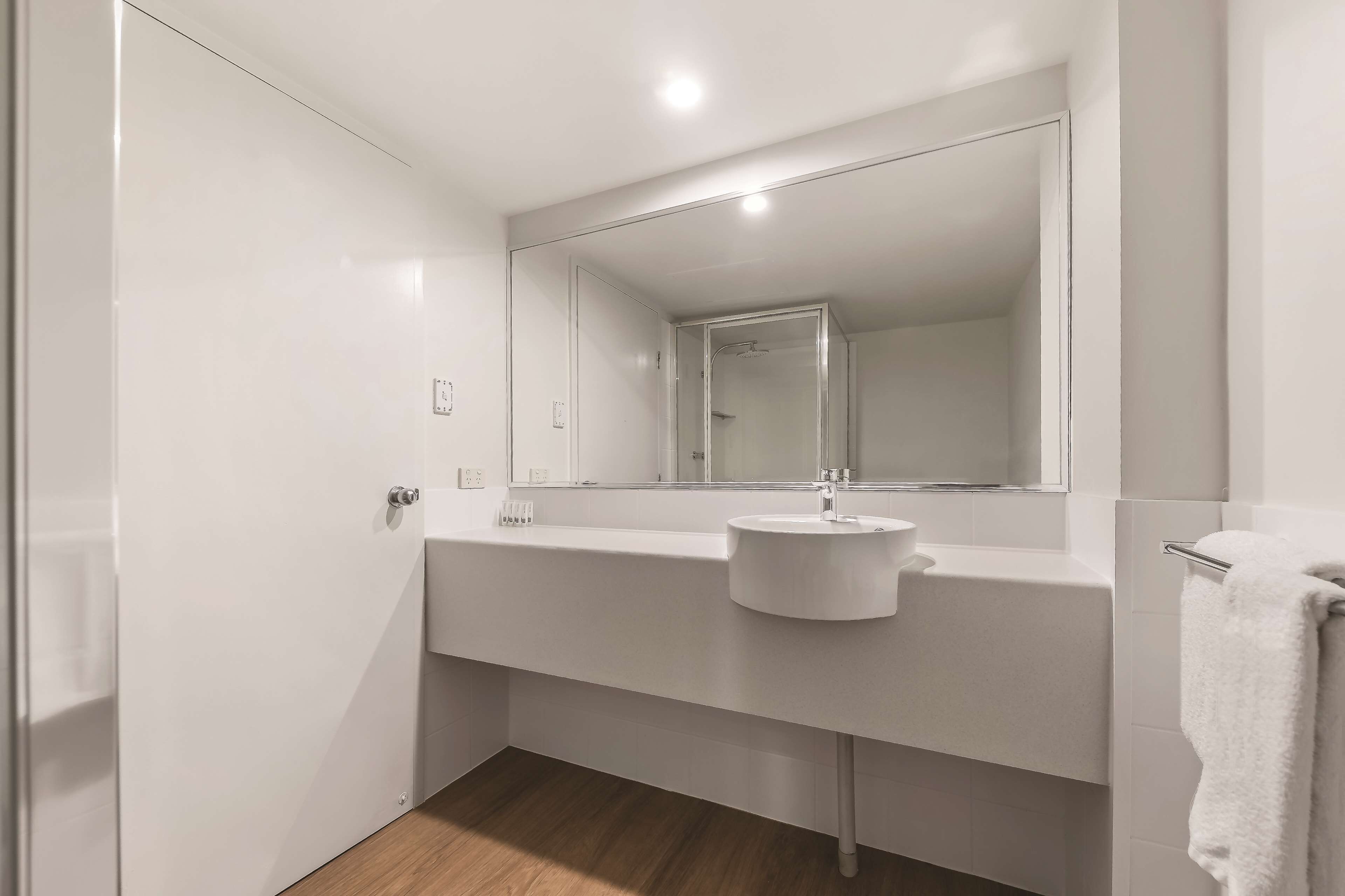 A modern bathroom with a white sink, mirror, and towel rack.