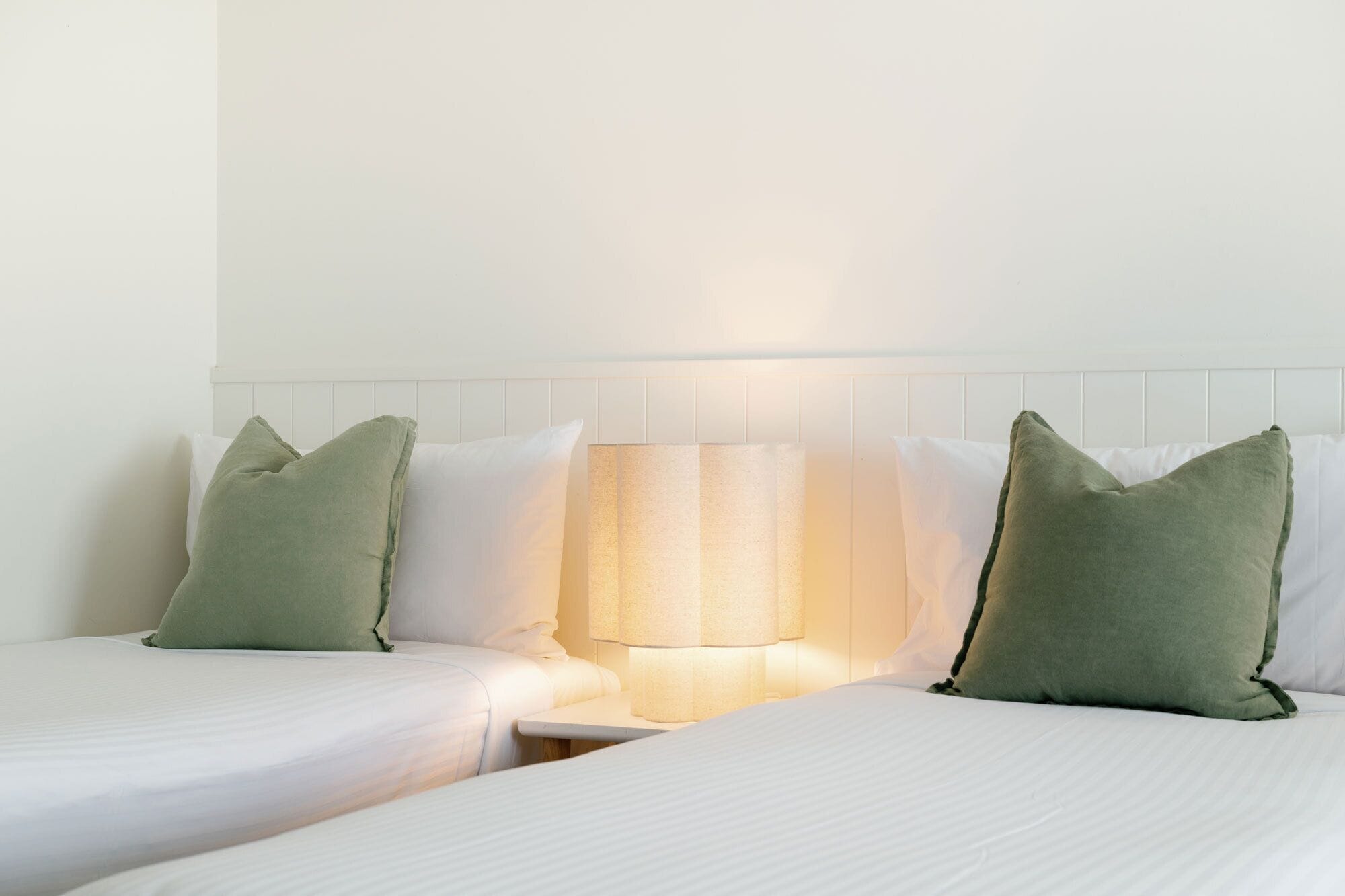 A hotel room with two beds, a nightstand, and a lamp.