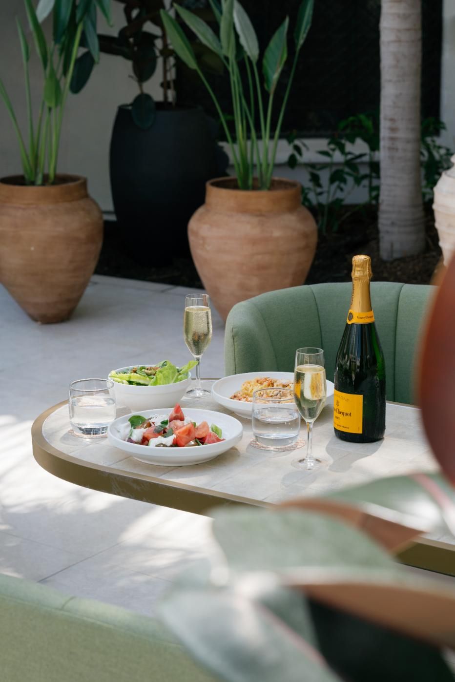 A dining table with a bottle of champagne, a glass, and plates of food.