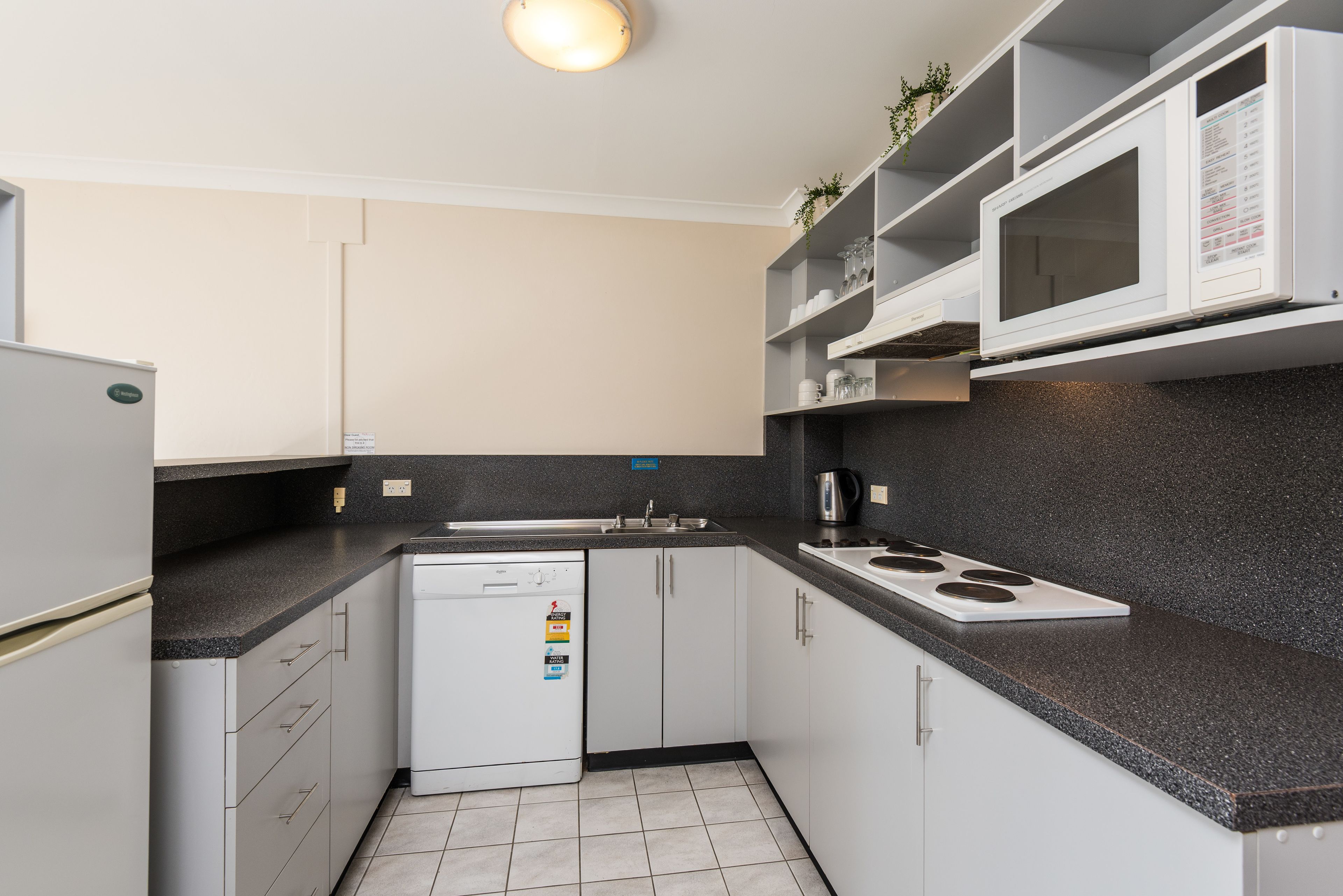 A modern kitchen with white cabinets, a black countertop, a built-in microwave, and a dishwasher.