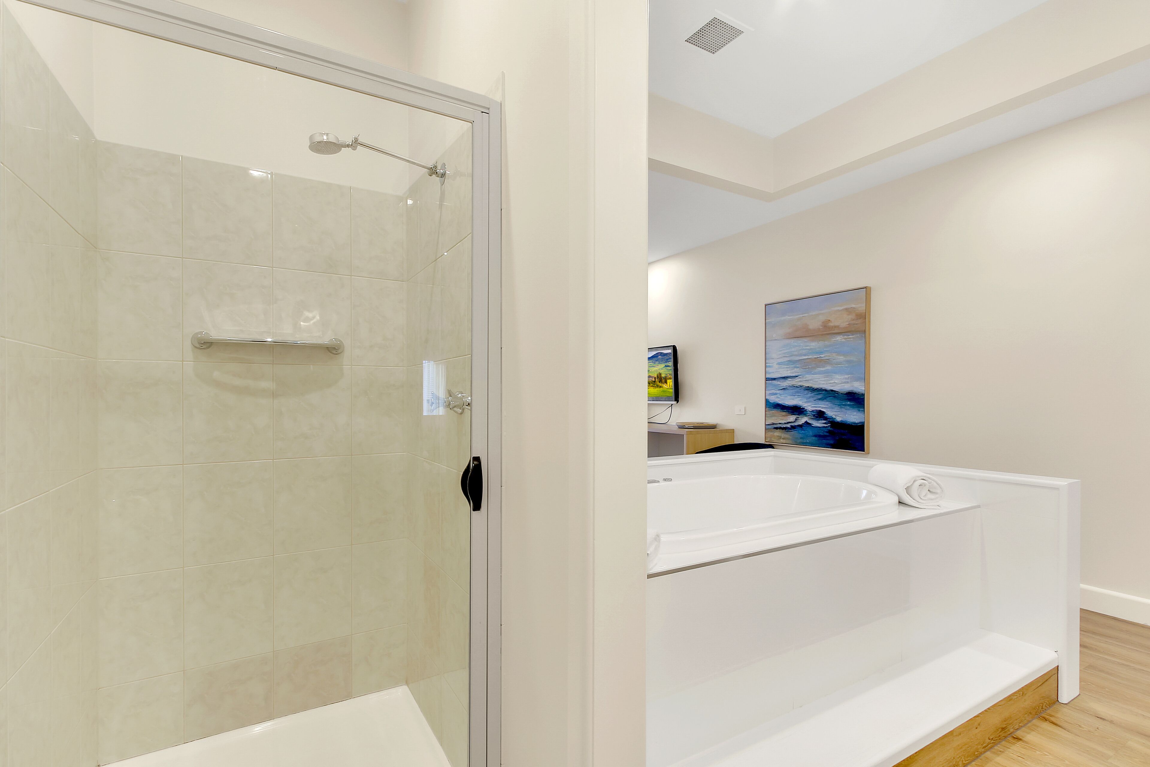 A modern bathroom with a glass-enclosed shower, a white bathtub, and a wooden floor.