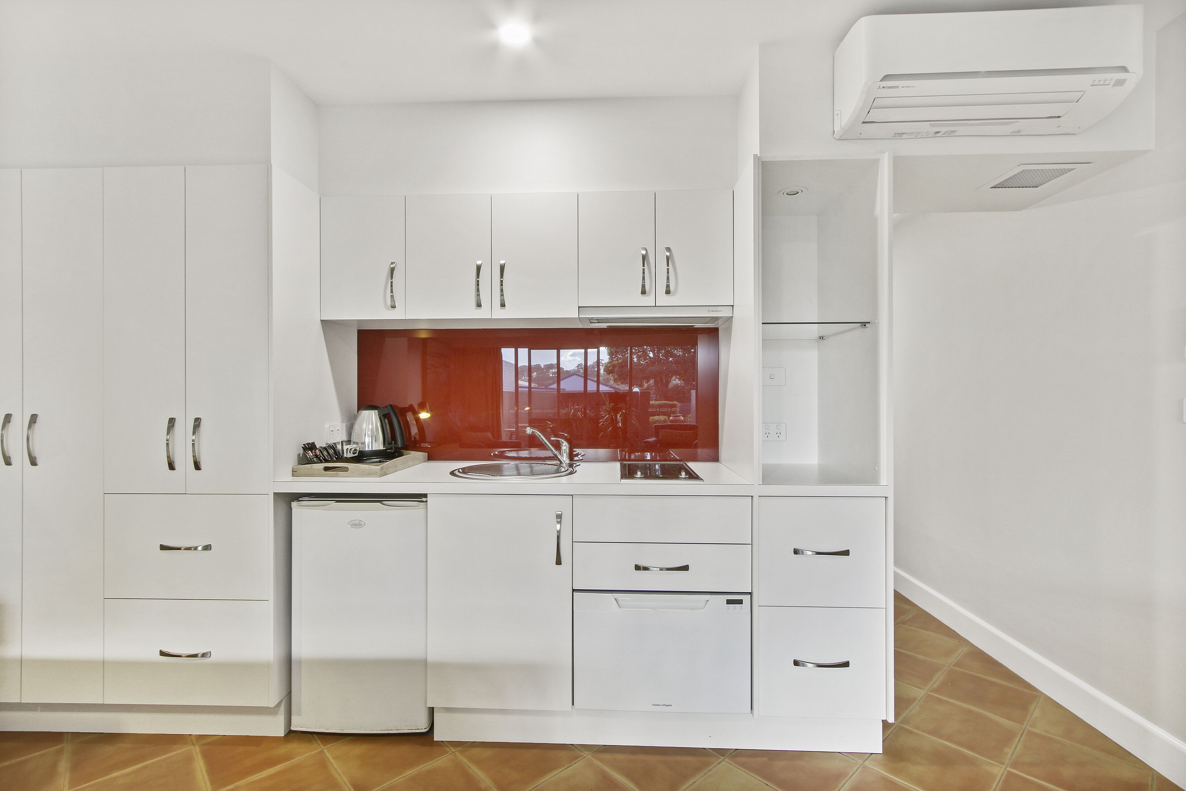 A modern kitchen with white cabinetry, a built-in dishwasher, and a window with a red frame.