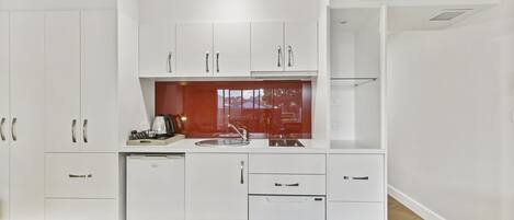 A modern kitchen with white cabinetry, a built-in dishwasher, and a window with a red frame.