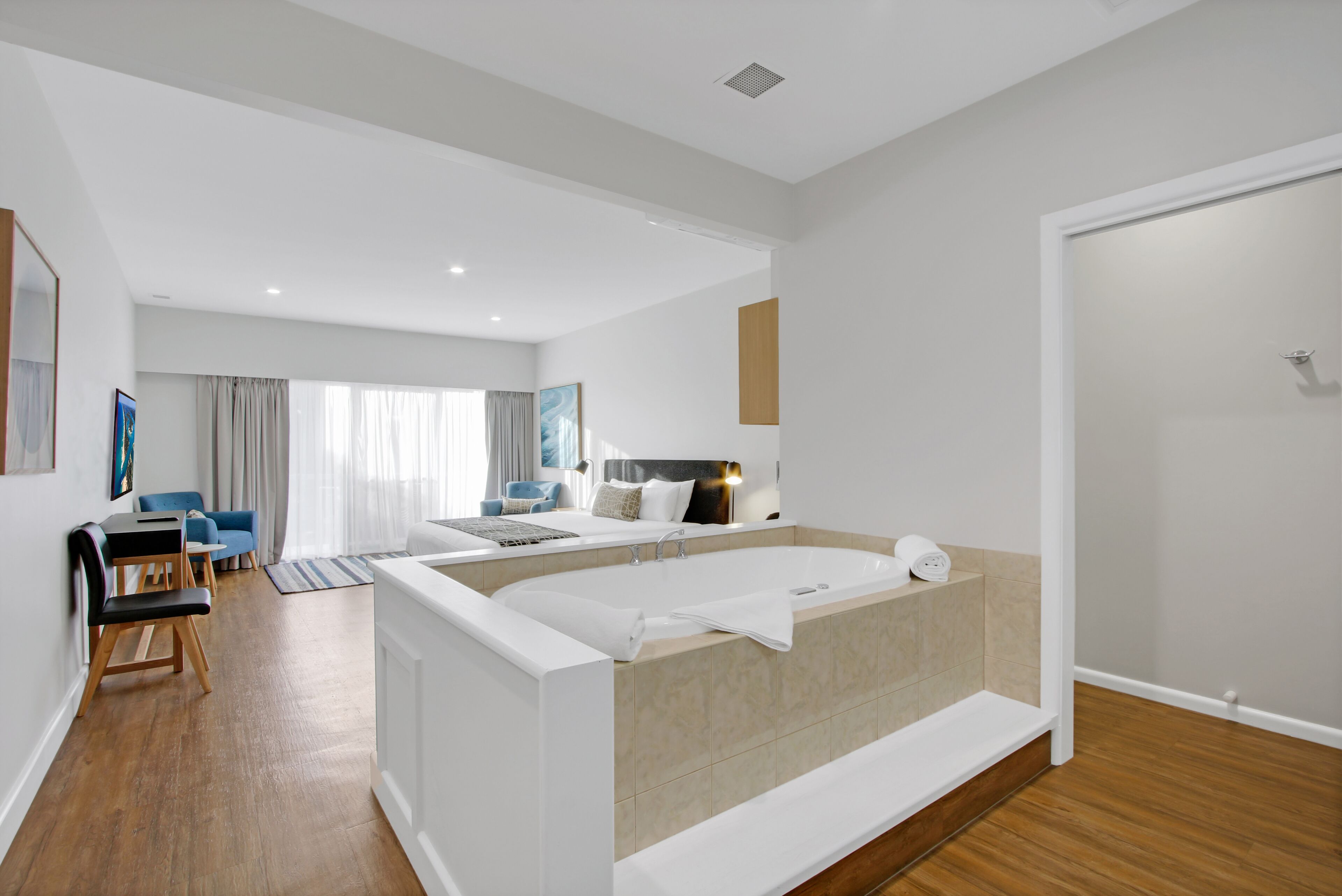 A modern hotel room with a large bathtub, a sitting area with a sofa and chairs, and a dining table.