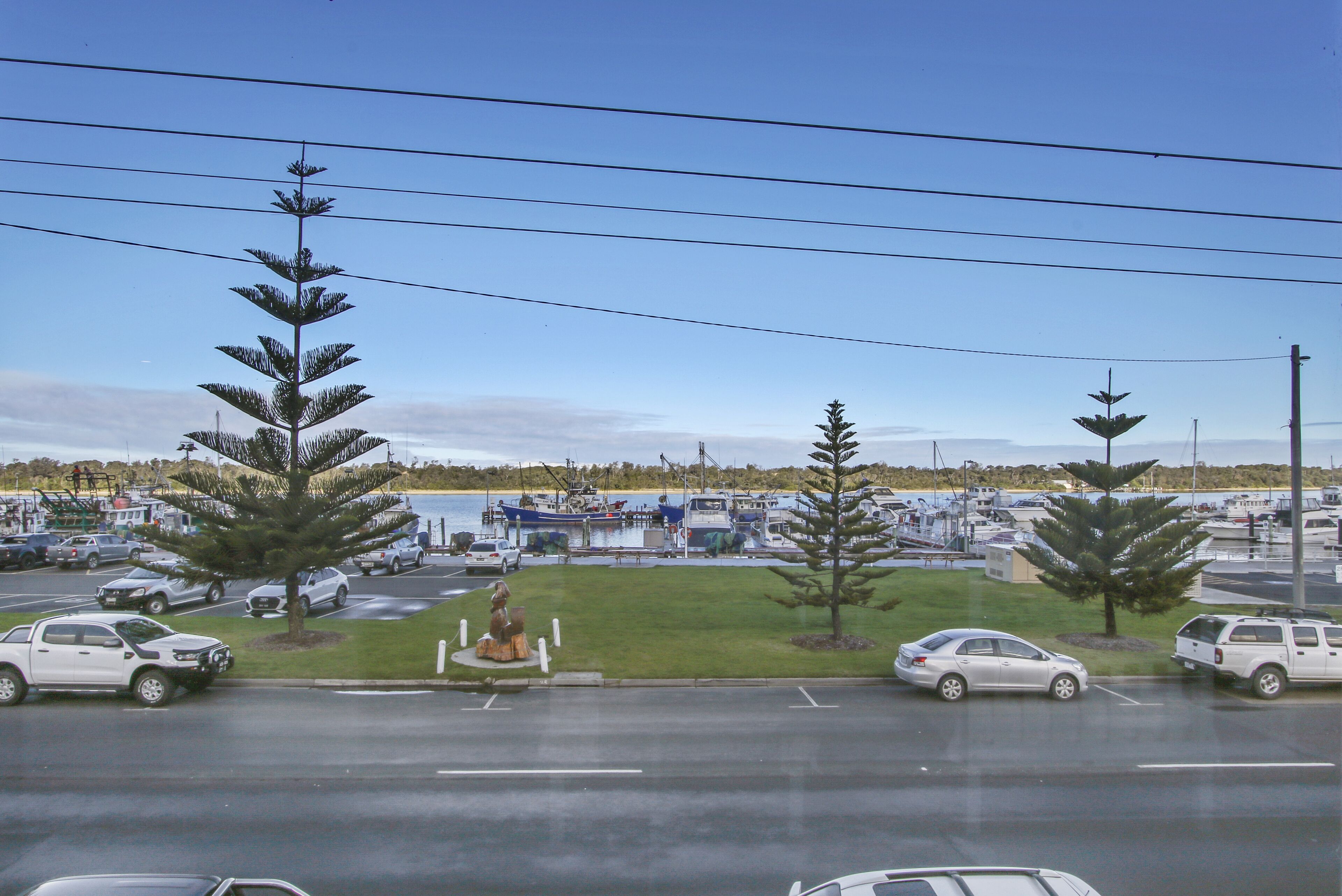A marina with boats docked, a parking lot with cars, and a statue in the foreground.