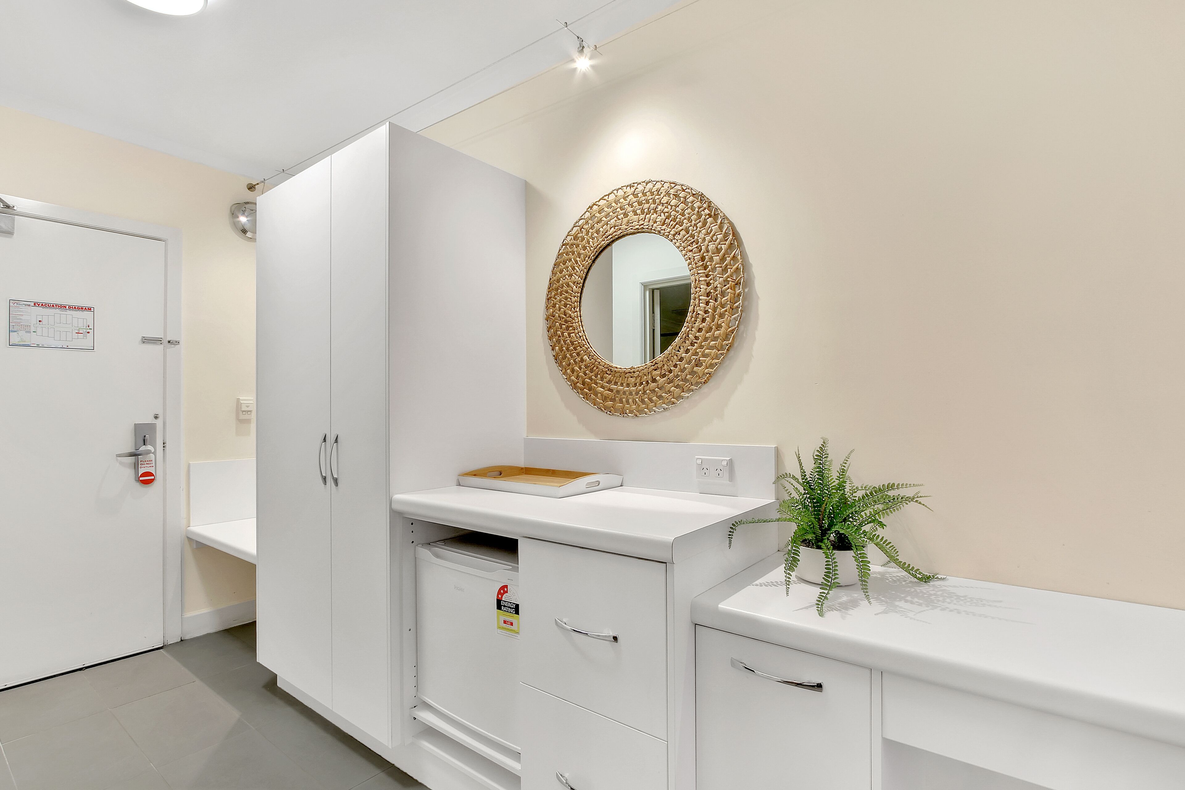 A clean, modern bathroom with a white sink, a mirror with a woven frame, and a potted plant.