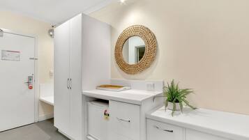 A clean, modern bathroom with a white sink, a mirror with a woven frame, and a potted plant.